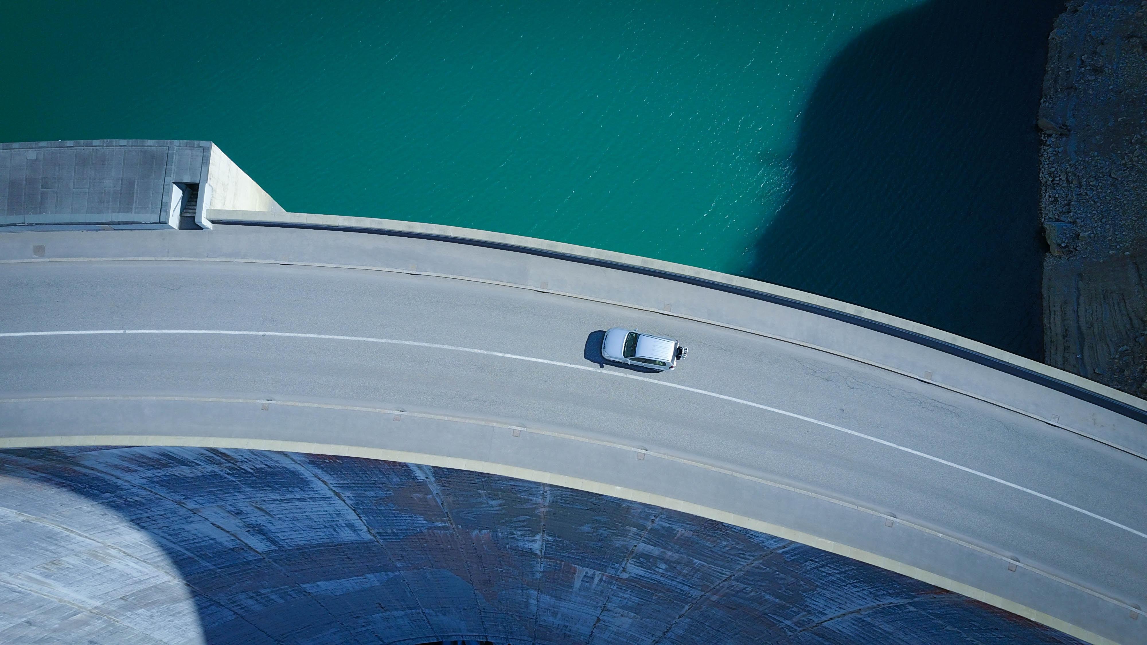 birds_eye_view_of_a_car_driving_along_the_top_of_a_dam