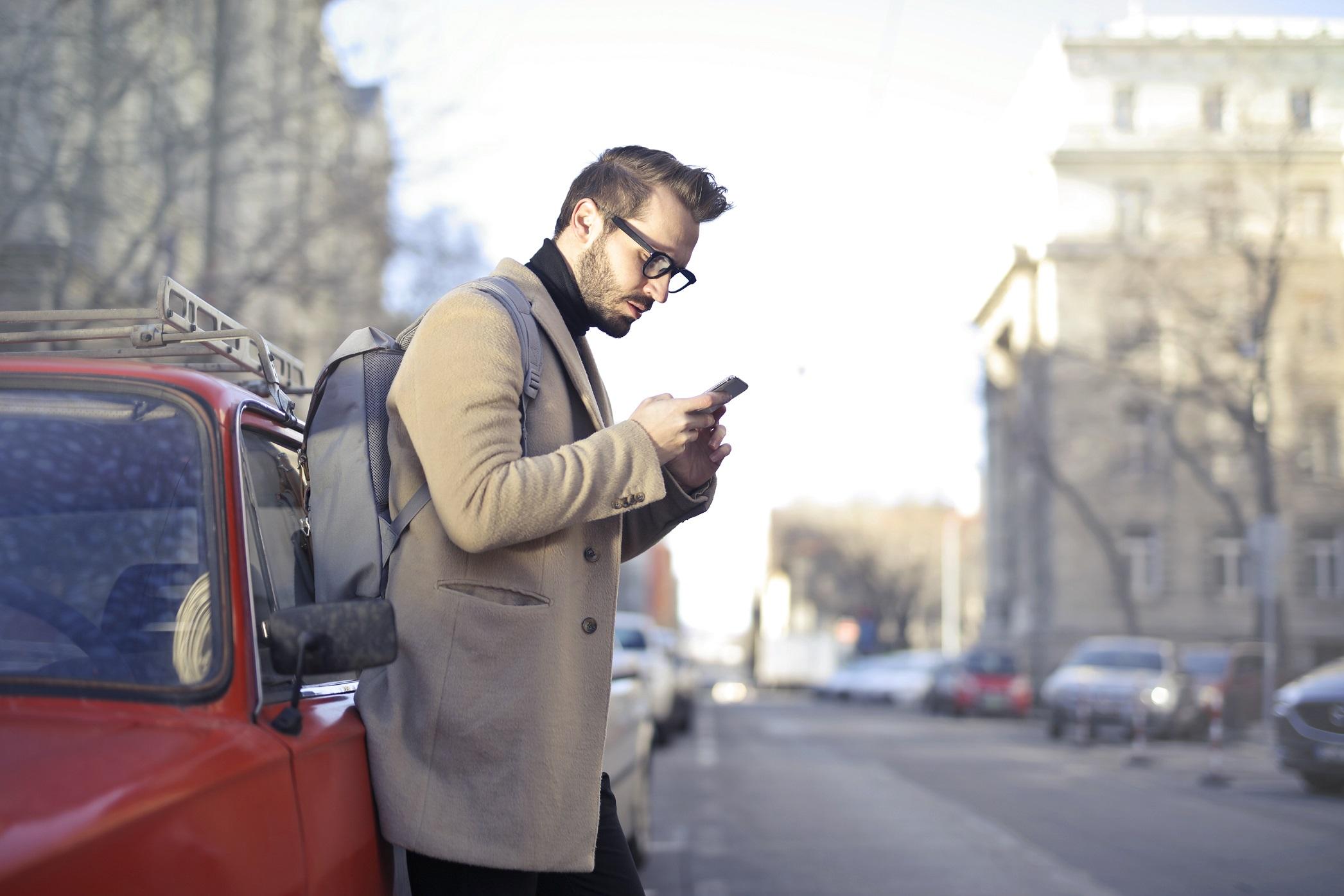 man_outside_looking_at_his_phone_while_leaning_on_car