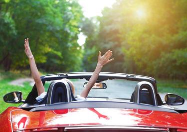 a_persons_hands_in_the_air_in_exclamation_in_a_convertable