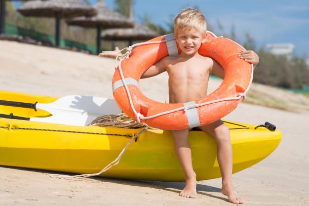 child_holding_a_lifering_on_abeach_next_to_a_kiak