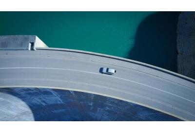 birds_eye_view_of_a_car_driving_along_the_top_of_a_dam