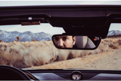 man_looking_into_his_rear_view_mirror_on_a_desert_road