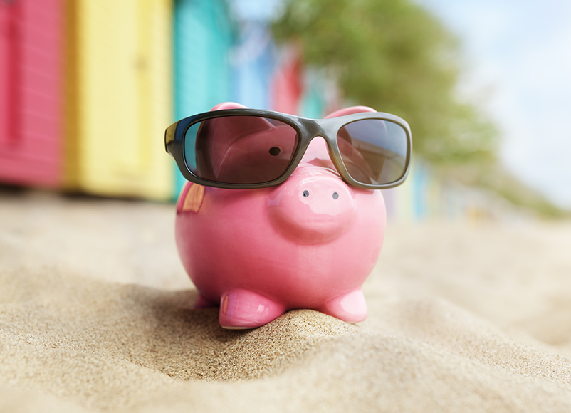 pink savings piggy bank in sunglasses sitting on the beach