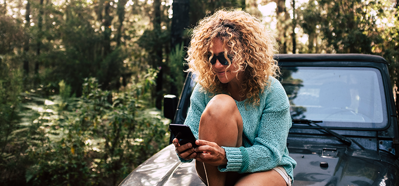 woman sitting down on car outside using phone